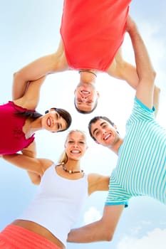 Low angle view of four friends embracing and looking at camera
