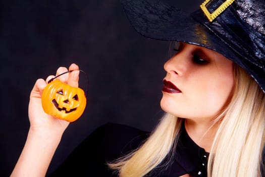 Image of black witch holding pumpkin candle and looking at it
