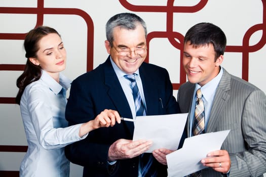 Portrait of happy businessmen looking into document at which elegant lady pointing during meeting