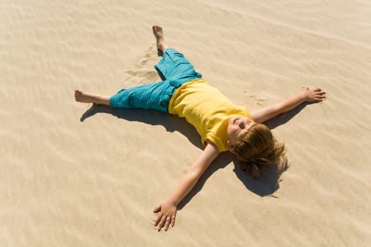 Above view of happy boy lying on sand and enjoying sunlight