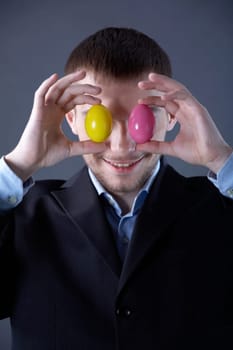 Portrait of smiling businessman holding colorful eggs in front of eyes