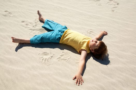 Above view of happy boy lying on sand and enjoying sunlight