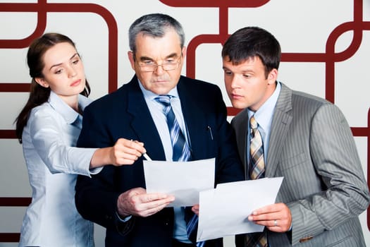 Confident woman pointing at paper in bosss hands with young businessman looking into it seriously standing near by