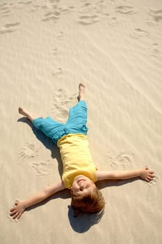 Above view of happy boy lying on sand and enjoying sunlight