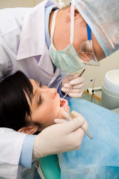 View from aside of young patient with open mouth while it being examined by dentist