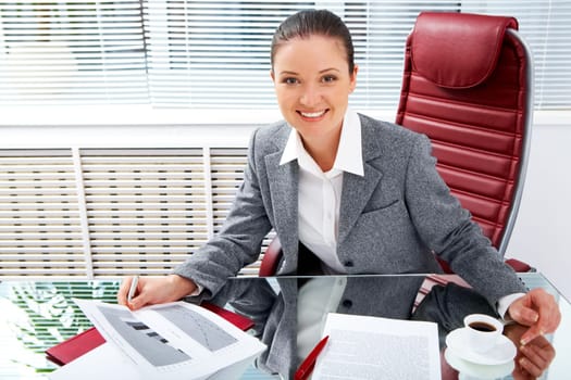 Portrait of successful businesswoman holding document while looking at camera with smile in office
