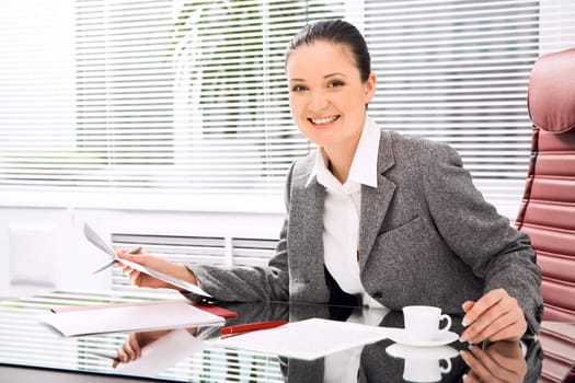 Portrait of successful businesswoman holding document while looking at camera with smile in office