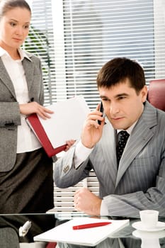 Portrait of confident boss talking on the phone with executive secretary standing near by