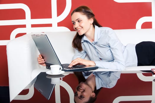 Photo of pretty business lady lying on sofa with laptop in front and looking at its monitor with smile