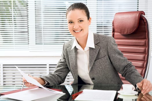 Portrait of successful businesswoman holding document while looking at camera with smile in office