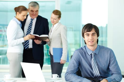 Portrait of confident leader looking at camera with working employees behind
