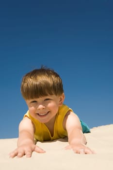 Happy boy lying on sand and looking at camera with smile during summer vacations