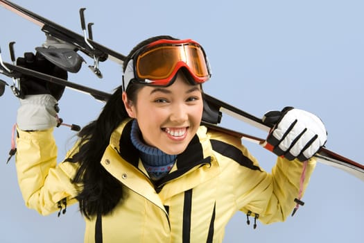 Portrait of smiling girl with sport glasses holding the skis on her back