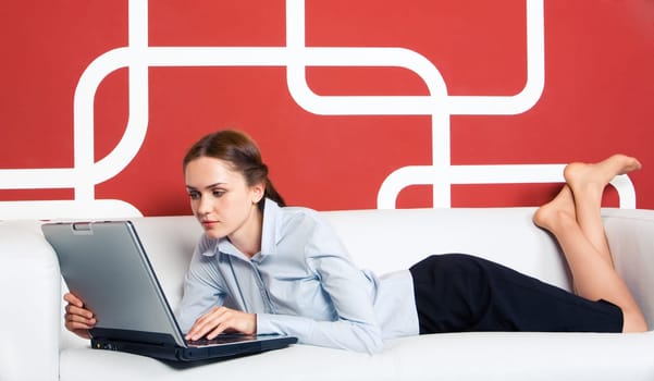 Image of serious girl typing on laptop on white sofa in the office