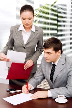 Portrait of serious boss signing contract with executive secretary near by