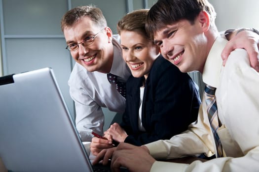 Three smiling businessmen looking at the laptop