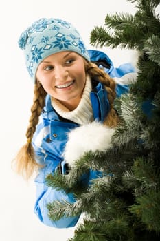 Portrait of young pretty woman peeping from Christmas tree
