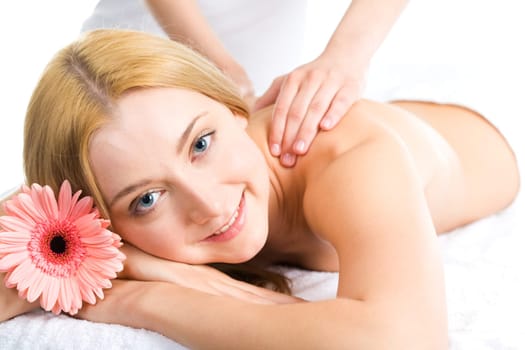Photo of smiling woman lying in the spa salon with a flower near by