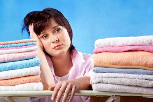 An upset woman sitting at heaps of ironed towels