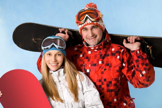 Portrait of happy couple with snowboards in hands looking at camera on blue background