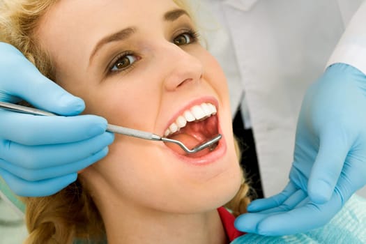 Close-up of young woman during inspection of oral cavity with help of hook and mirror