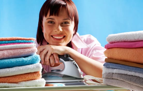 Portrait of young female with iron between two stacks of colorful towels smiling at camera