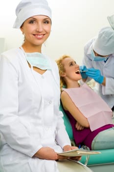 Portrait of young professional looking at camera on background of her colleague and patient