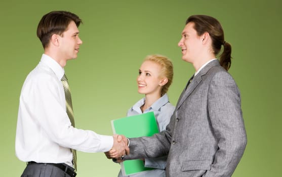 Portrait of successful business partners handshaking while pretty female looking at one of them