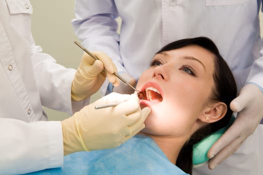 Photo of female patient with open mouth while her teeth being examined supported by assistant