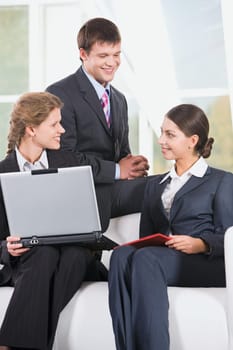 Portrait of three smiling business people sitting on the sofa and discussing a working questions