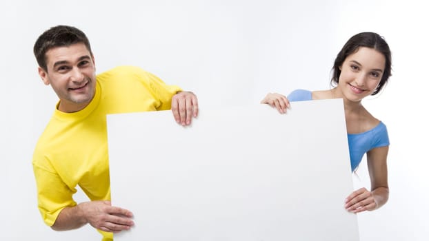 Smiling couple holding blank poster and looking at camera on white background