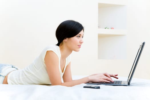 Photo of teenage girl lying on bed and pressing laptop keys at home