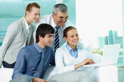 Portrait of several colleagues looking at laptop screen in office