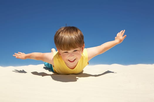 Happy boy lying on sand with outstretched arms on beach