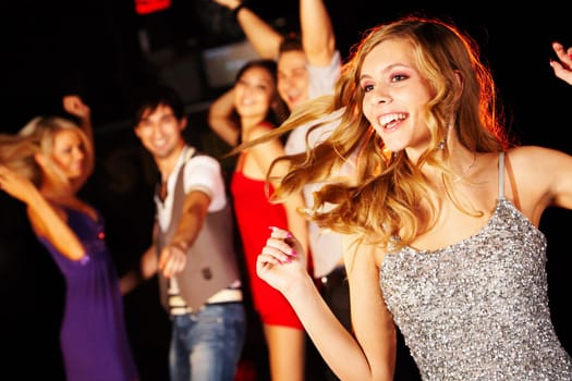Portrait of joyous girl dancing at party on background of happy teens