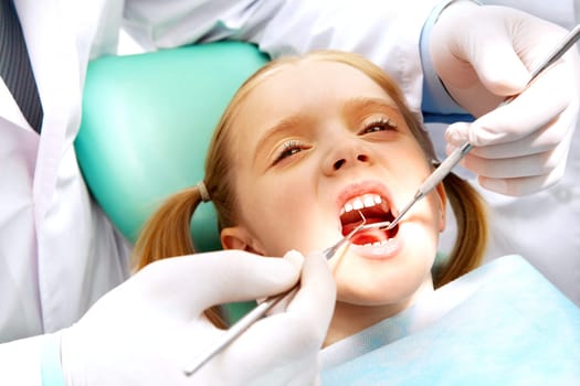 Photo of small girl with open mouth while it being examined by dentist