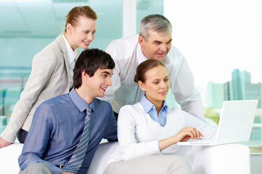 Portrait of several colleagues looking at laptop screen in office