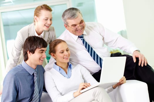 Portrait of several colleagues looking at laptop screen in office