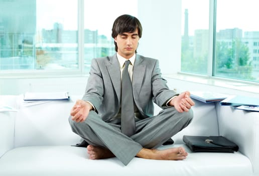 A young businessman meditating on sofa in office