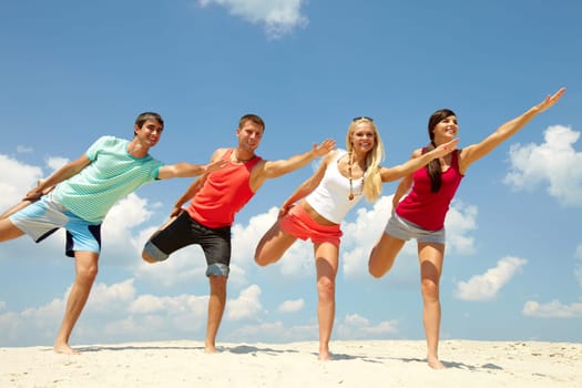 Four happy friends doing exercise on the beach