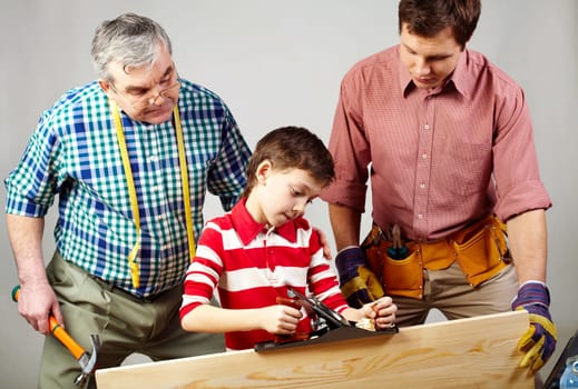 A boy working with plane under his father and grandpas supervision