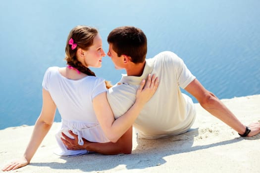 Backs of peaceful couple sitting on sandy shore and looking at each other