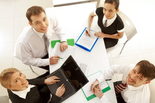 Several white collar workers looking upwards at camera from their workplaces