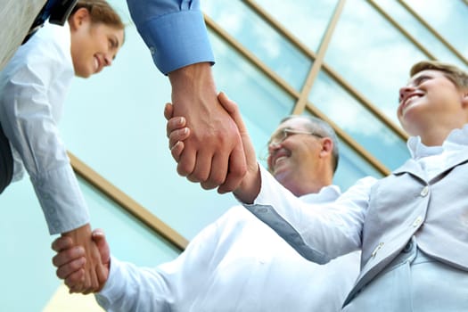 Below view of rows of happy partners handshaking outdoors on background of modern building