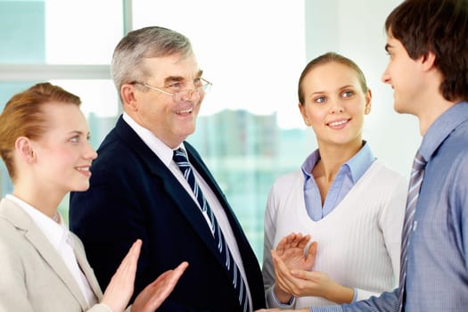 Photo of successful businessmen handshaking after striking deal with applauding women near by