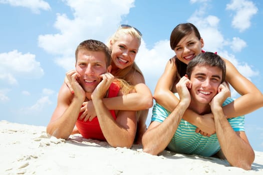 Two happy couples lying on sand and looking at camera