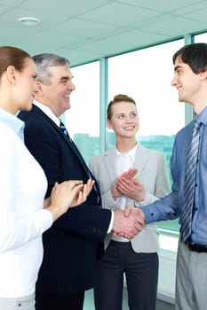 Photo of successful businessmen handshaking after striking deal with applauding women near by
