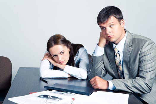 Portrait of pensive businesswoman and businessman sitting at the table with documents on it