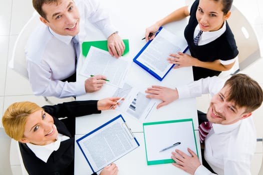 Several white collar workers looking upwards at camera from their workplace