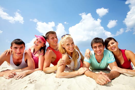Three happy couples lying on sand and looking at camera